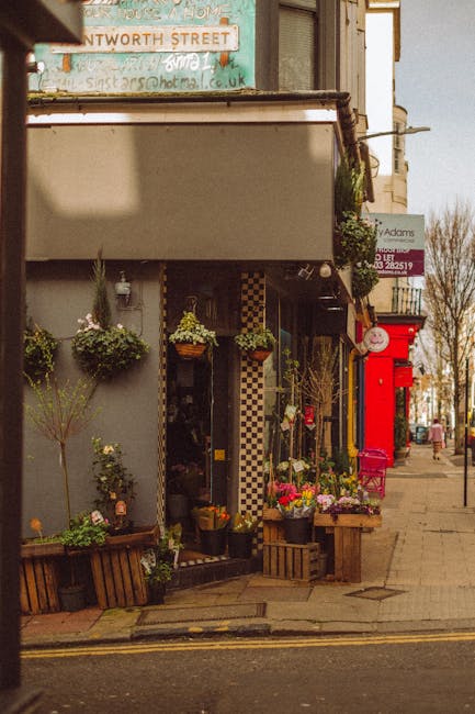 The image showcases the exterior of a flower shop on a street in Brunswick Park Road N11, with a display of floral arrangements and potted plants arranged outside the shop entrance. The flowers includ